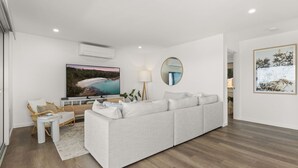 Un salon moderne avec un canapé gris, un téléviseur à écran plat, un miroir rond et un tableau encadré accroché au mur.
