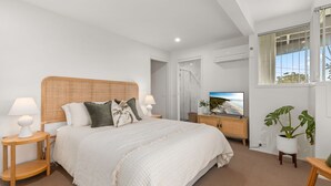 Une chambre moderne avec un grand lit, des lampes de chevet, une télévision et une vue sur l’extérieur.
