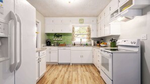 A kitchen with white cabinets, a green backsplash, a clock, and a window with curtains. - Family Fave_PutPut_Sleeps 10_Near DT LS Walkable (Lee's Summit)