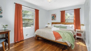 A bedroom with a wooden bed, two bedside tables, a ceiling fan, and windows with orange curtains. - Family Fave_PutPut_Sleeps 10_Near DT LS Walkable (Lee's Summit)