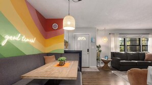 A modern living room with a wooden coffee table, grey sofa, and a black leather couch. A neon sign reads "good times!" on the wall. - Family Fave_PutPut_Sleeps 10_Near DT LS Walkable (Lee's Summit)