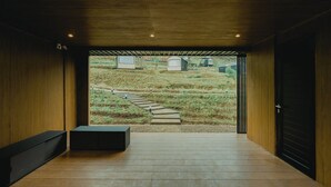 A modern interior with a wooden floor, a bench, and a view of a garden with a stone pathway. - Bobocabin Gunung Mas (Cisarua)