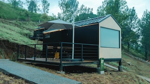 A modern, two-story cabin with a balcony, situated on a hillside with a view of the surrounding forest. - Bobocabin Gunung Mas (Cisarua)