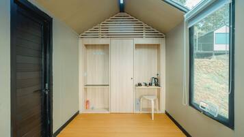 Habitación pequeña con techo inclinado, piso de madera, un escritorio con silla y una ventana con vista a una ladera.