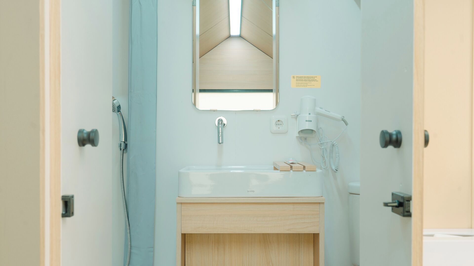 Un baño con un lavabo blanco, un espejo, un cabezal de ducha de mano y un secador de pelo.