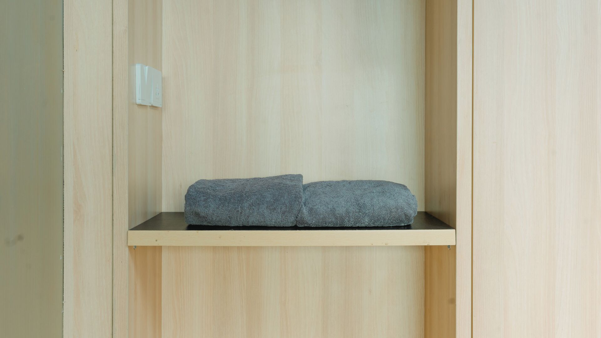 A wooden cabinet with a shelf holding a folded gray towel.