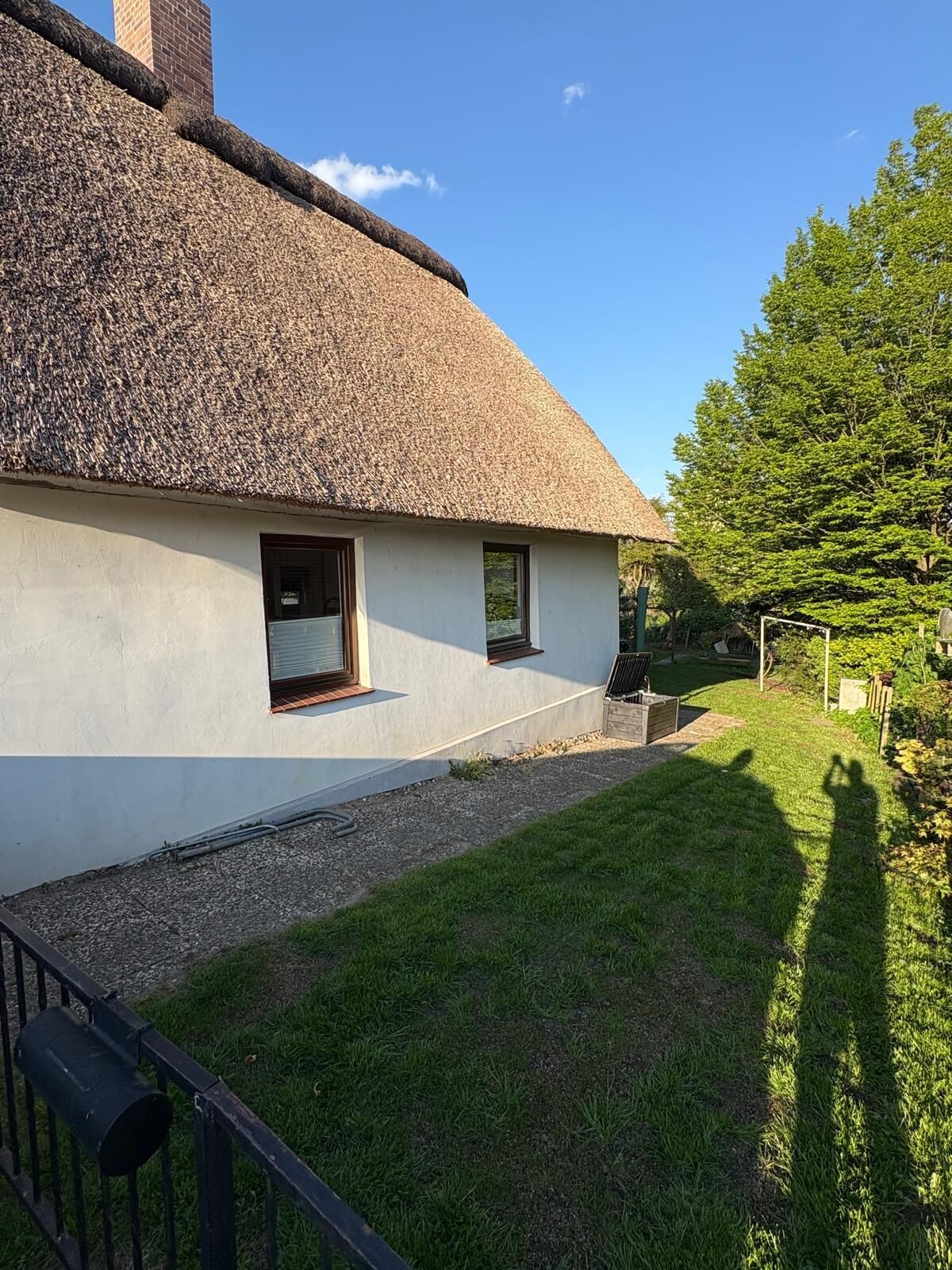 Une maison à toit de chaume, aux murs blancs, avec une petite fenêtre et une cour couverte d’herbe.
