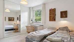 Een slaapkamer met een bed, een bureau, een stoel, een spiegel en een raam met gordijnen.