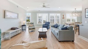 Uma sala de estar espaçosa com um sofá cinzento, uma poltrona azul e uma mesa de centro de vime.
