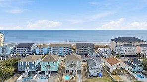 A beachfront hotel with multiple buildings, including a large blue building with a pool and a smaller white building with a pool. - Anchor Down Luxury Ocean View Beach House w Pool (North Myrtle Beach)
