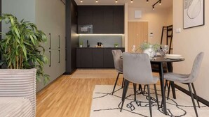 A modern kitchen with dark cabinets, a microwave, and a dining area with a table and chairs. - Stylish Apartment with Balcony | Air Conditioning and Parking (Warszawa)