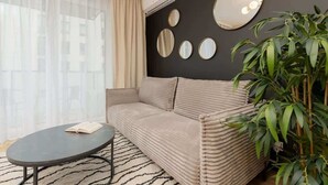 A modern living room with a beige sofa, a round coffee table, and a large mirror on the wall. - Stylish Apartment with Balcony | Air Conditioning and Parking (Warszawa)