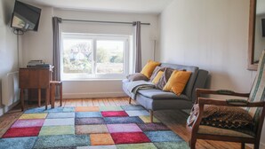 Una sala de estar con un sofá, una silla, una mesita y un televisor montado en la pared.