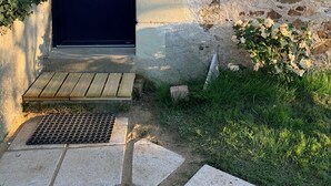 Entrada de un edificio con una puerta oscura, paredes de piedra, un escalón de madera y una rejilla de metal.