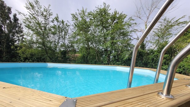 Una terraza de madera con piscina, rodeada de árboles.