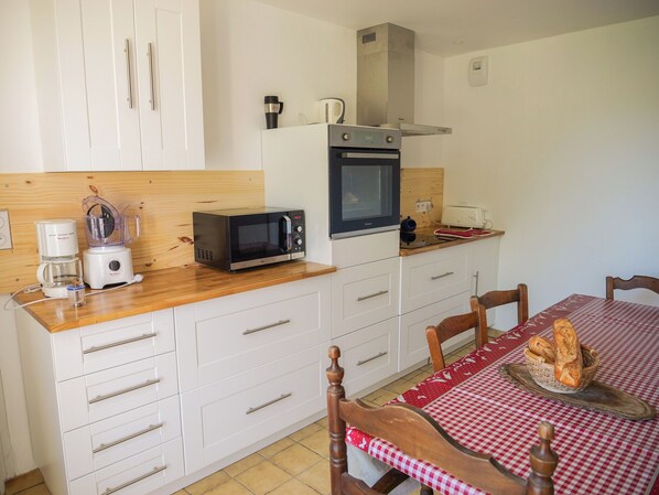 A compact kitchen with a microwave, toaster, and coffee maker. There is a wooden countertop, white cabinets, and a dining table with a checkered tablecloth.
