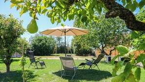 Un patio trasero con un columpio, dos sillas de jardín y una mesa bajo un paraguas grande.