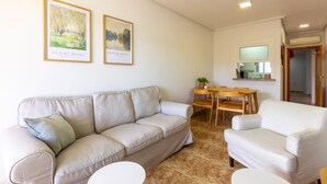 Una sala de estar con un sofá color beige, un sillón blanco, una mesita redonda y dos cuadros enmarcados en la pared.