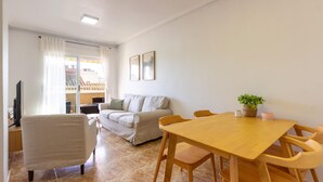 Una sala de estar con un sofá, una mesa de comedor de madera con sillas, un televisor y una planta en maceta.