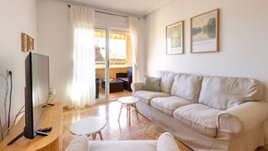 Una sala de estar con un sofá color beige, un televisor de pantalla plana, una mesita y dos cuadros en la pared.