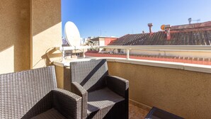 Un balcón con sillas de mimbre, una antena parabólica y vistas a edificios y una grúa al fondo.