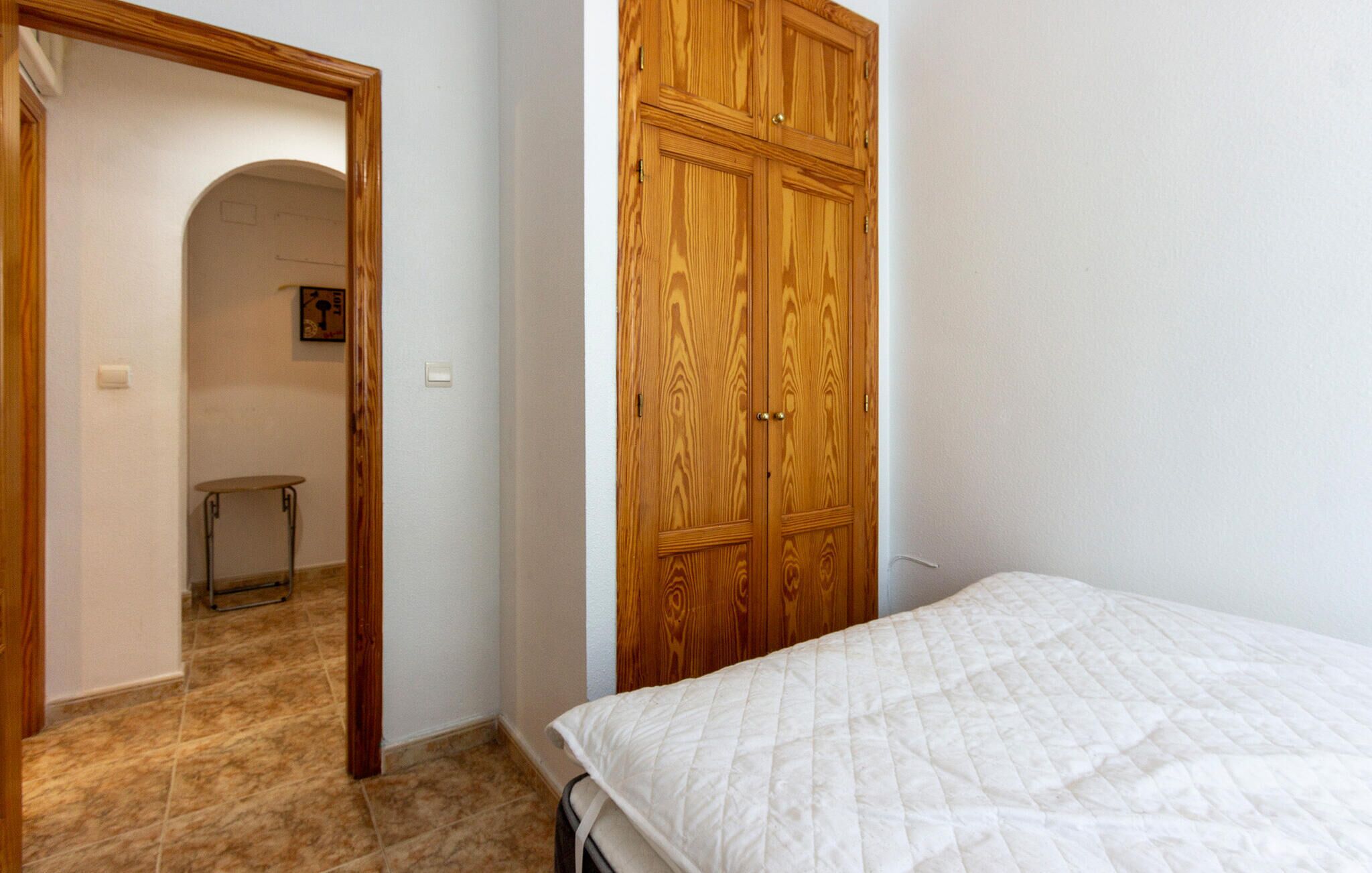 A bedroom with a wooden wardrobe, a bed with a quilted cover, and a small table.