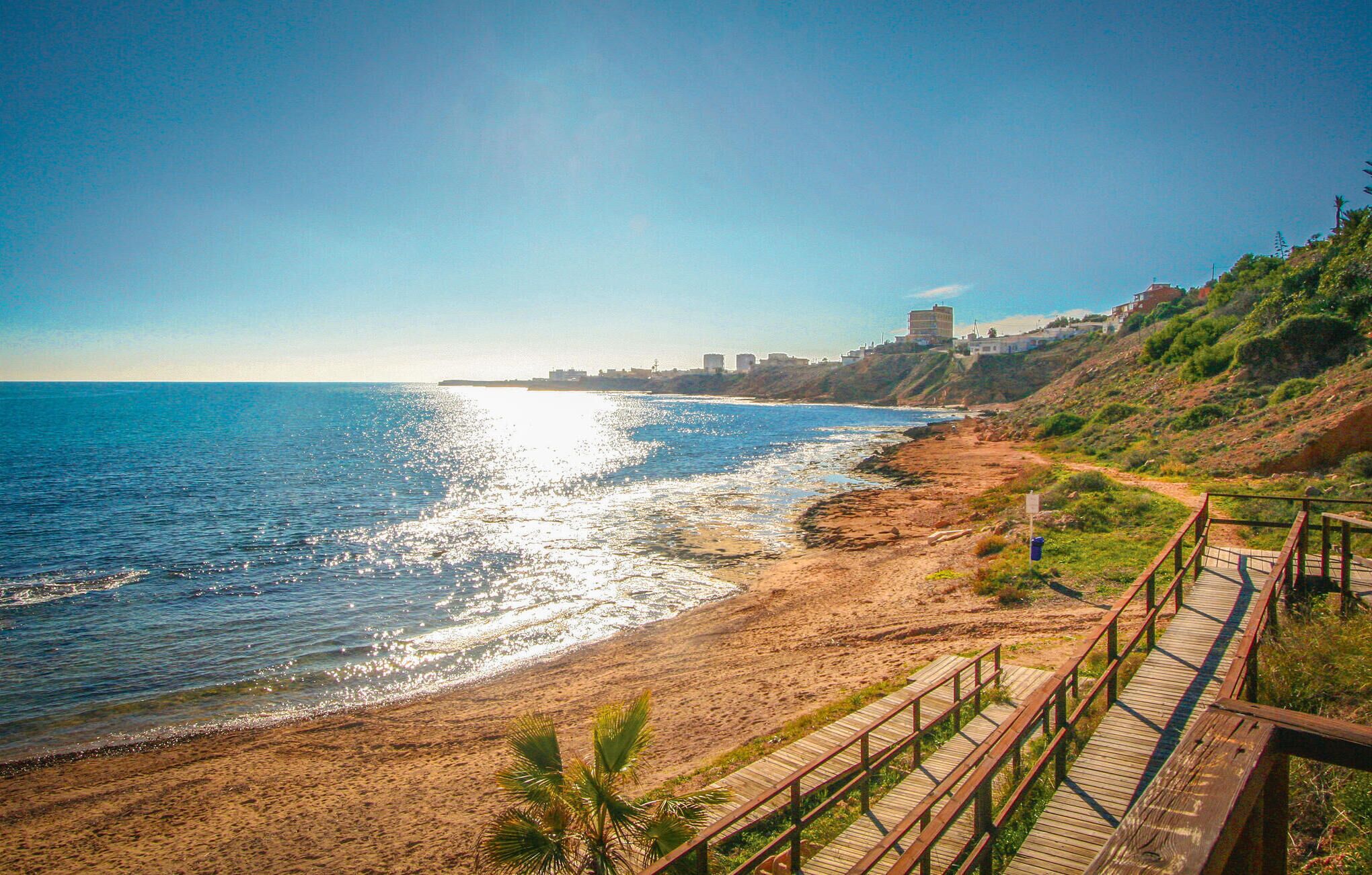 Una playa costera con un paseo marítimo de madera que llega a la orilla.