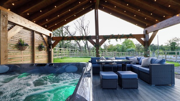 Un espacio al aire libre cubierto con un jacuzzi, asientos y una pérgola de madera.