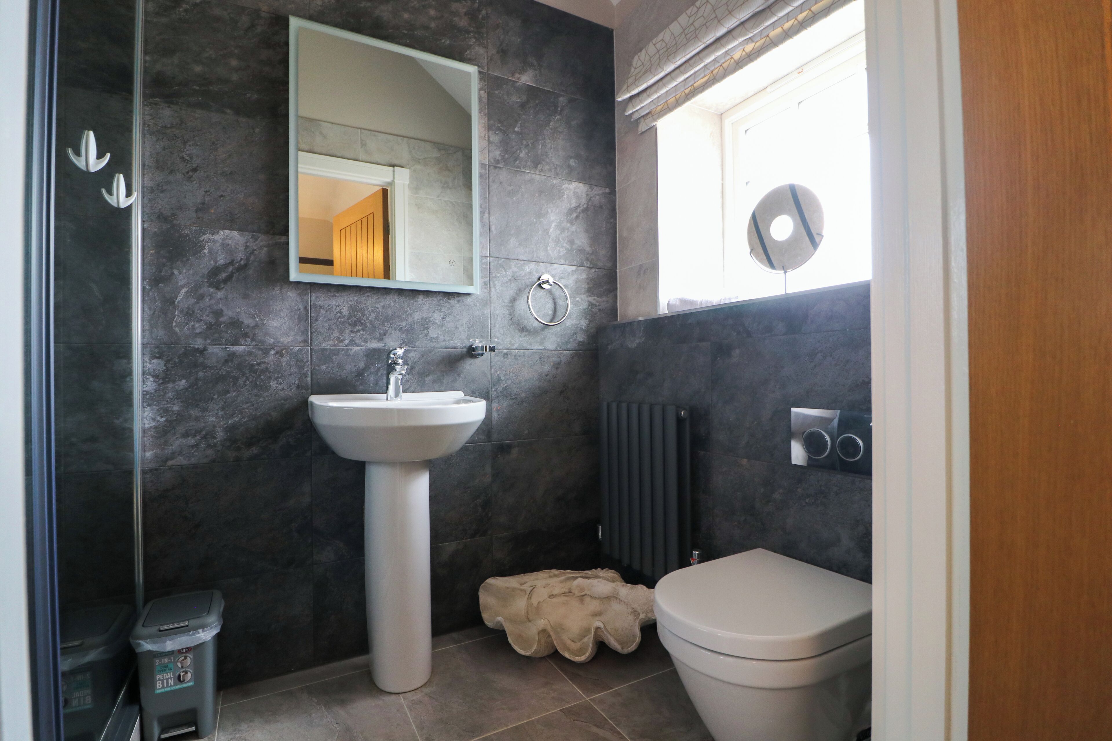 A modern bathroom with a pedestal sink, a toilet, a radiator, and a mirror.