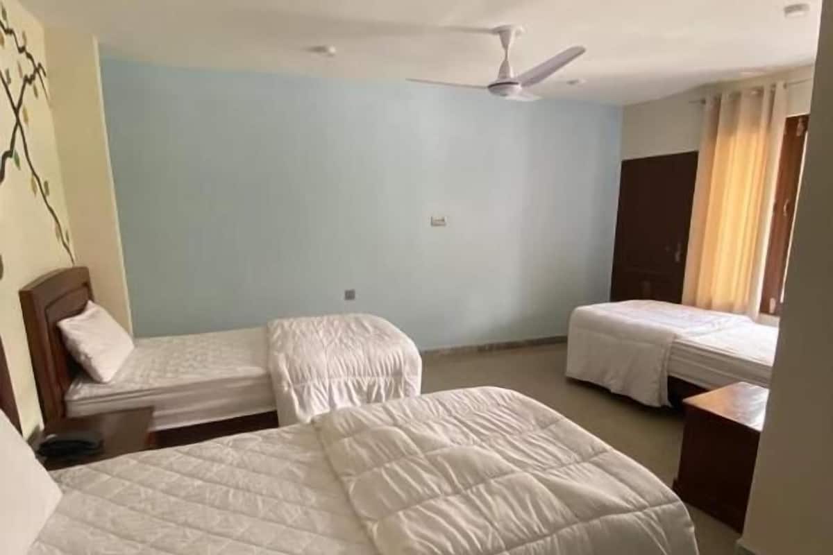 A hotel room with two single beds, a ceiling fan, and a window with curtains.