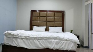 Ein ordentlich bezogenes Bett mit Holz-Kopfteil und weißer Bettwäsche in einem Zimmer mit hellen Wänden und Fliesenboden.