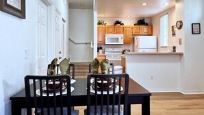 A dining area with a table and chairs, a kitchen with wooden cabinets and white appliances, and a hallway with white doors.