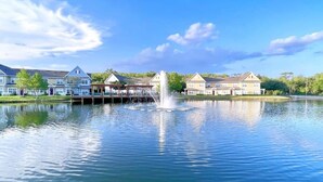 A tranquil lake with a fountain in the center, surrounded by residential buildings with a gazebo and a dock.