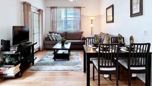 A living room with a sofa, coffee table, TV, and dining area with chairs and table.