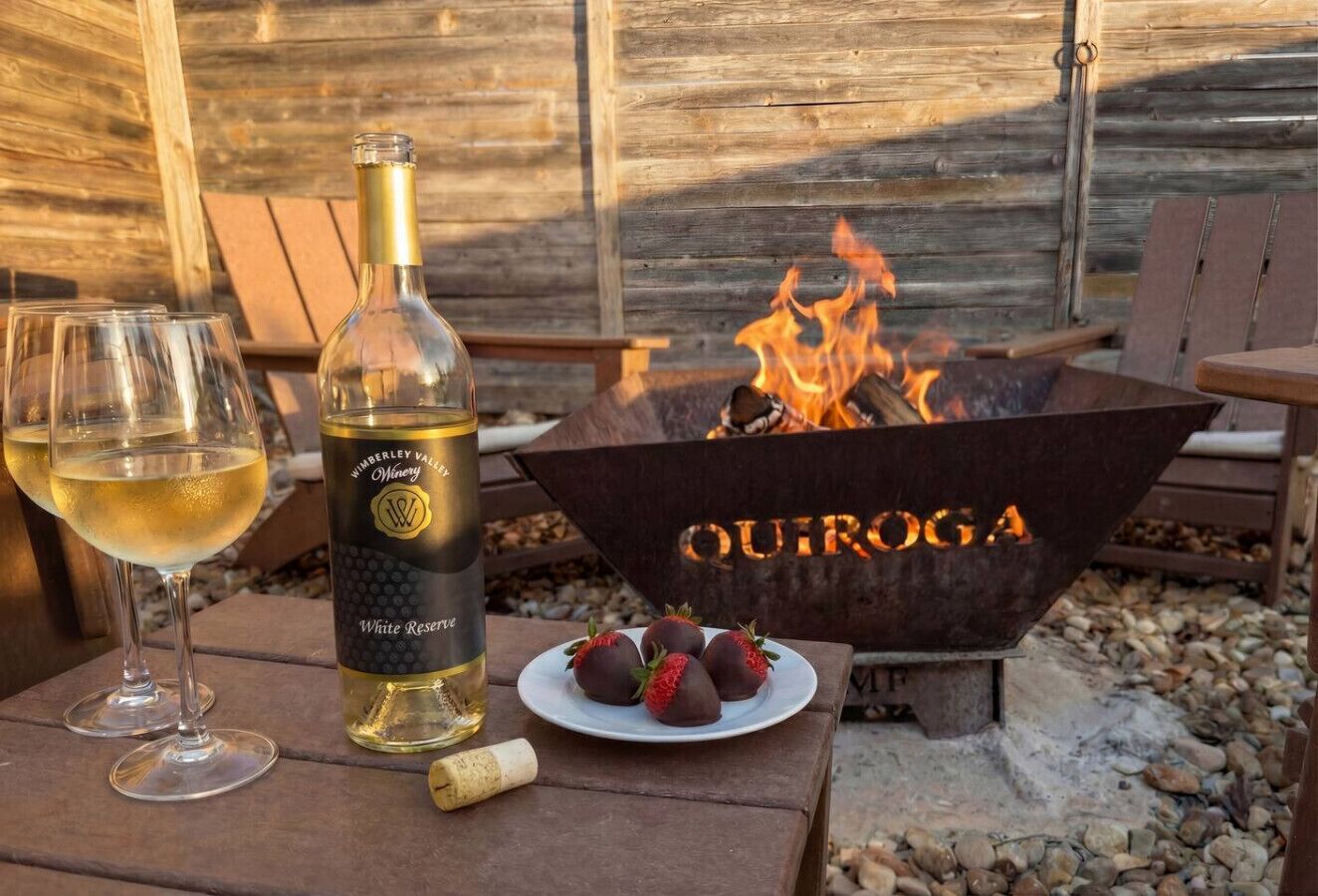 Una botella de vino, copas, fresas y un brasero con el nombre 'OUIROGA' sobre una mesa de madera.