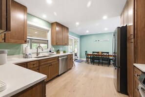Una cocina moderna con armarios de madera, un refrigerador de acero inoxidable y una zona de comedor con mesa y sillas.