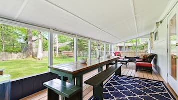 A covered patio with a wooden table and benches, a patterned rug, and a view of a backyard.
