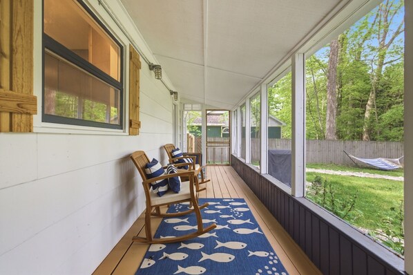Un portico coperto con sedie a dondolo, un tappeto azzurro con motivi a pesce e vista su un giardino con un'amaca.