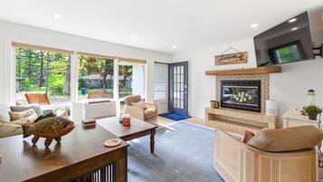 A modern living room with a fireplace, comfortable seating, and large windows offering a view of the outdoors.