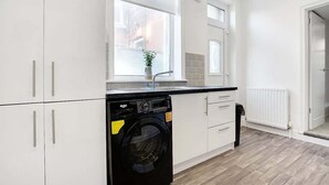 A modern kitchen with white cabinetry, a built-in washing machine, and a window with a view. - Spacious 4BR retreat Eden Vale | by Stay With Us (Sunderland)