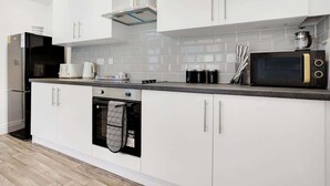 A modern kitchen with white cabinets, a black microwave, a coffee maker, and a kettle. - Spacious 4BR retreat Eden Vale | by Stay With Us (Sunderland)