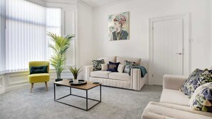 A living room with a yellow armchair, a white sofa, a coffee table, and a large window with blinds. - Spacious 4BR retreat Eden Vale | by Stay With Us (Sunderland)