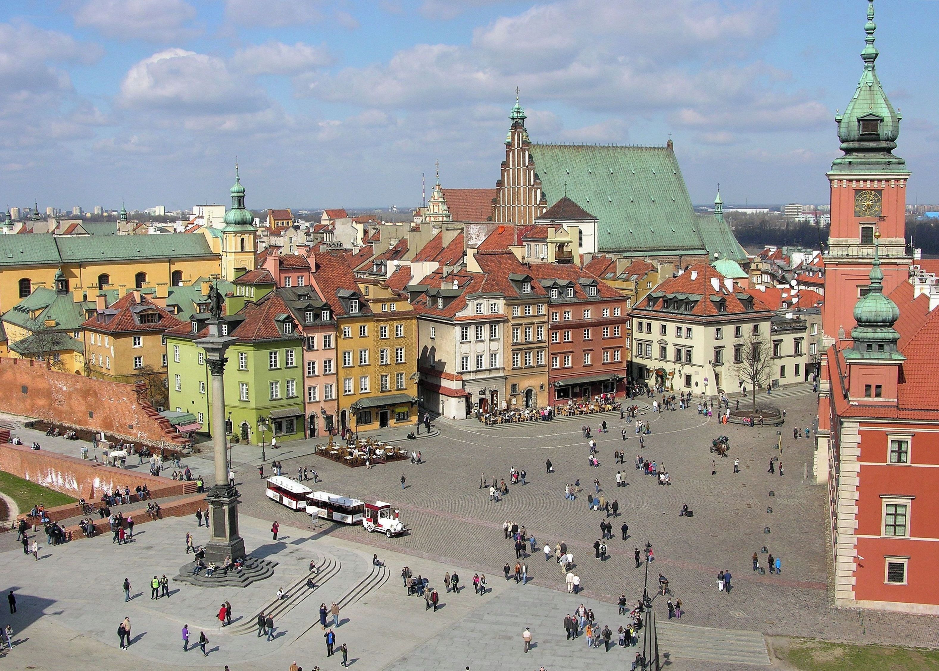 A historic square with colorful buildings, a prominent clock tower, and a tram.