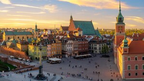 Ett historiskt torg med ett centralt monument, omgivet av färgglada byggnader och ett markant klocktorn.