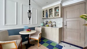 A compact kitchen with a dining area, featuring a round table, two chairs, a hanging light fixture, and a door with a decorative panel. - Seven Seas Côte d'Azur by PSR (Sattahip)