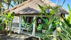 A thatched-roof bungalow with a porch, surrounded by tropical vegetation. - Exlusive Lodge in a Boutique Hotel (Selong Belanak)