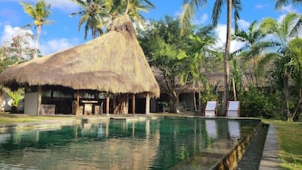 A pool area with a thatched-roof structure, palm trees, and a clear sky. - Exlusive Lodge in a Boutique Hotel (Selong Belanak)