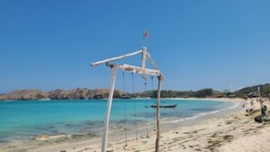 A beach with a simple structure, clear turquoise water, and distant hills. - Exlusive Lodge in a Boutique Hotel (Selong Belanak)