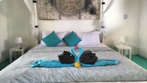 A neatly made bed with a blue and white patterned bedspread, two teal pillows, and a folded towel arrangement on the bed. - Exlusive Lodge in a Boutique Hotel (Selong Belanak)