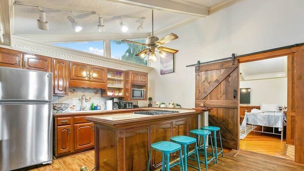 A kitchen with wooden cabinets, a stainless steel refrigerator, a central island with stools, and a ceiling fan. - Enormous Historic Treme Pad by French Quarter (New Orleans)